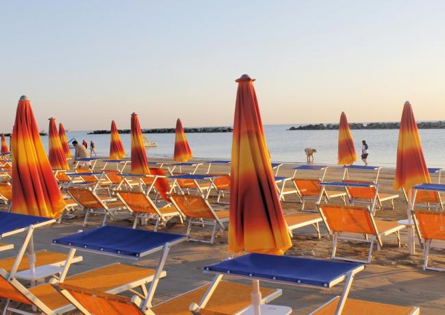 Beach with orange umbrellas and empty deck chairs at sunset.