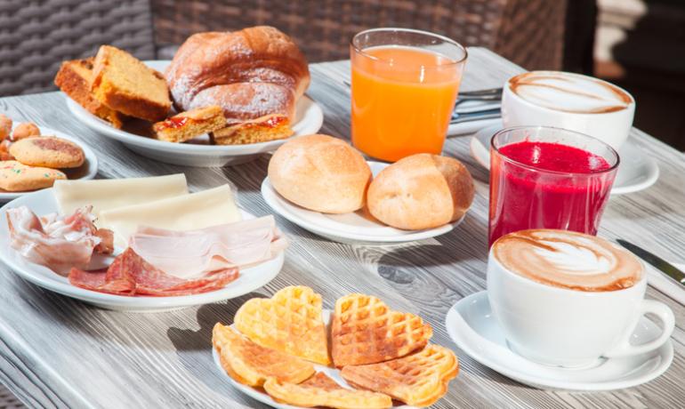 Breakfast with coffee, juices, pastries, and cold cuts on table.
